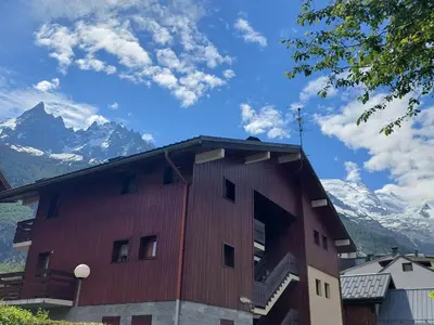 a red building with snow capped mountains in the background at Chamonix: Charmant 2 pièces avec parking proche centre - FR-1-517-66 in Chamonix-Mont-Blanc