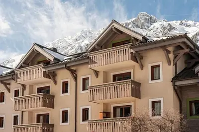 a large building with balconies and snow covered mountains at Résidence La Ginabelle - maeva Home - 2 Pièces 4 Personnes Prestige MAE-1307 in Chamonix-Mont-Blanc