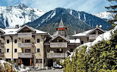a large building with snow covered mountains in the background at Résidence La Ginabelle - maeva Home - 2 Pièces 4 Personnes Prestige MAE-1307 in Chamonix-Mont-Blanc