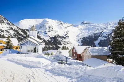 a church covered in snow with mountains in the background at Les Chalets de Flaine Hameau - maeva Home - Chalet 5 Pièces 8 Personnes - Prestige MAE-3655 in Flaine