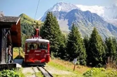 a red train traveling down the tracks near a mountain at Emeraude, petit cocon proche des pistes in Saint-Gervais-les-Bains