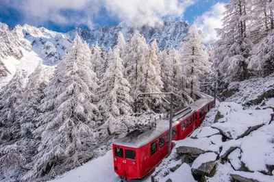 a red train traveling through the snow covered mountains at Chalet Altura- 5 Bedrooms - Jacuzzi and Sauna - By Cozee Rentals in Chamonix-Mont-Blanc