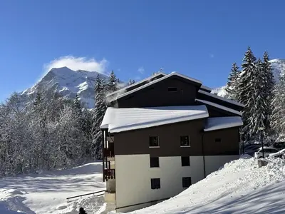 a building in the snow with a mountain in the background at Studio cabine rénové près ski bus, 4 couchages - FR-1-572-301 in Arâches-la-Frasse