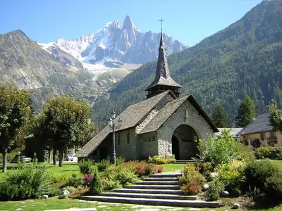 a church with a steeple with mountains in the background at La Ferme des Praz apartment - Chamonix All Year in Chamonix-Mont-Blanc