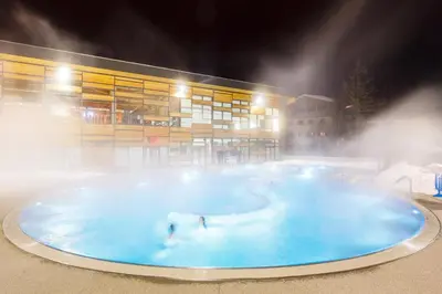 two people swimming in a pool in front of a building at Lara Megeve Jaillet proche du village Parking in Megève