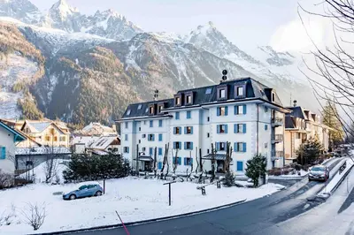 a large white building on a snowy street with mountains at Le Paradis 28 Apartment- Chamonix All Year in Chamonix-Mont-Blanc