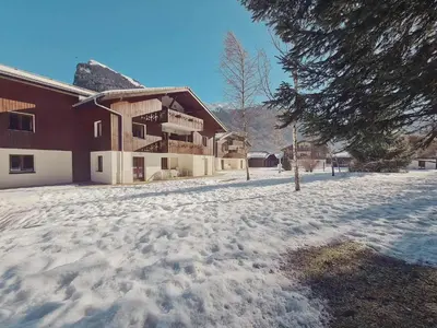 a snow covered yard next to a building with a house at Appartement familial avec piscines à Samoëns - FR-1-624-103 in Samoëns