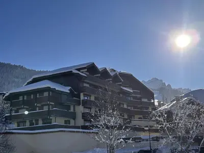 a building covered in snow with the sun behind it at Studio rénové pour 4 personnes, centre station, proche pistes et commodités - FR-1-572-24 in Arâches-la-Frasse